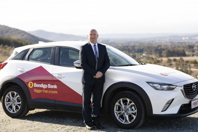 Bryan Dacey standing in front of Bendigo Bank car.