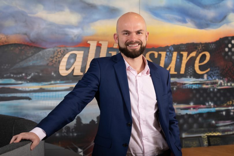 Tate Harris standing in front of allinsure sign. 