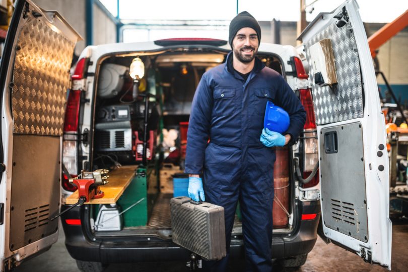 Tradie standing in front of van holding tools.