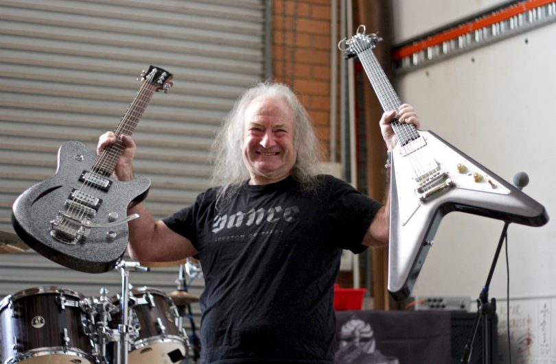Rusty Vance holding two custom guitars in his Fyshwick workshop.